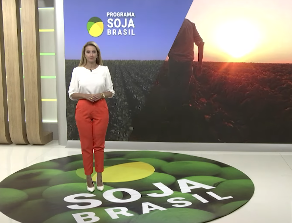 Apresentadora com camisa branca e calça laranja no estúdio do Soja Brasil