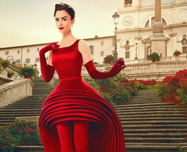 A imagem mostra uma moça descendo uma escadaria. Com um vestido vermelho, a moça usa acompanhamentos no visual que seguem a mesma cor do vestido