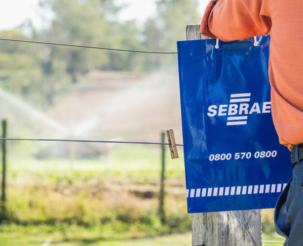 Homem segurando uma sacola do Sebrae e está olhando para o campo