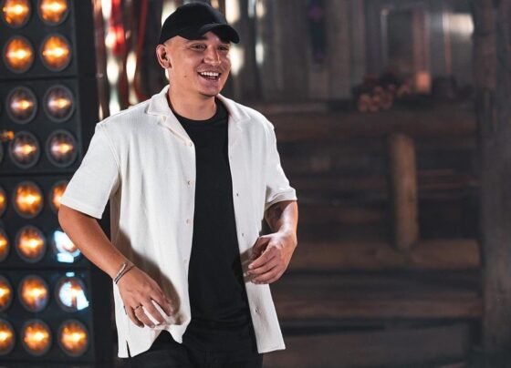 João Gomes posa com uma camiseta preta, blusa branca e boné preto - Metrópoles