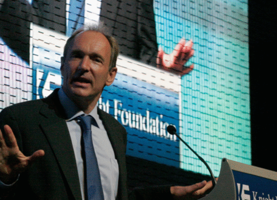 Fotografia colorida mostra Tim Berners-Lee, criador do protocolo HTTP, em uma apresentação. Ele veste terno e fala em um púlpito