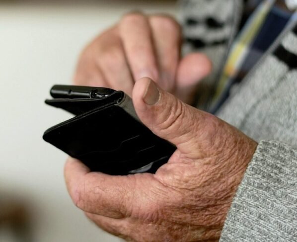 Foto de uma mão de uma pessoa idosa segurando um celular