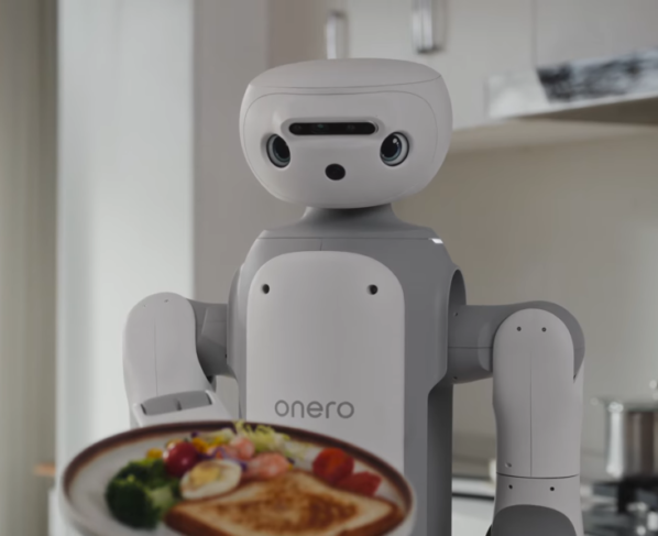 Plano detalhado de um robô humanoide branco e cinza, identificado com a inscrição "onero" no torso. A cabeça é arredondada, com olhos grandes e expressivos e um sensor horizontal na testa. O robô segura um prato de comida em primeiro plano, contendo uma torrada, ovo cozido, brócolis e tomates cereja. O cenário de fundo é uma cozinha moderna e clara, com armários brancos e um fogão, mantendo o foco principal na face e na ação do robô.