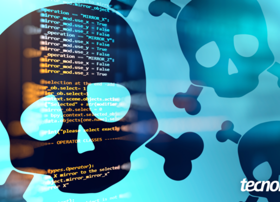 Imagem mostra crânios e ossos cruzados brancos e translúcidos sobre um fundo escuro com linhas de código de programação em azul claro. Os crânios representam pirataria, ataque hacker e perigo cibernético. Na parte inferior direita, o logotipo do "Tecnoblog" é visível.