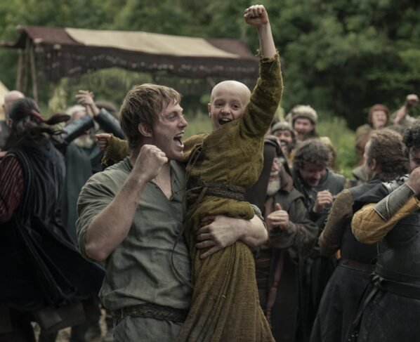 Homem segura criança careca no colo em cena da série O Cavaleiro dos Sete Reinos - Metrópoles