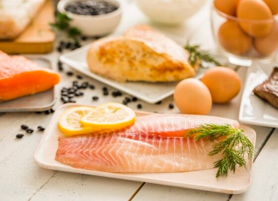 Peixe tilápia cru no prato, frango e ovos no fundo - Metrópoles