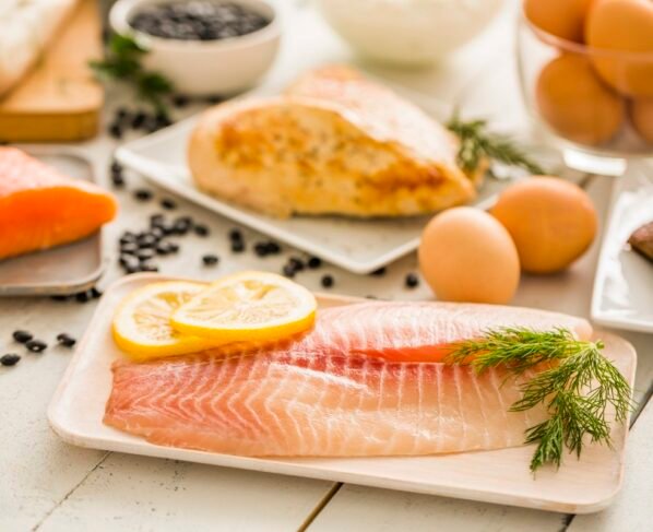 Peixe tilápia cru no prato, frango e ovos no fundo - Metrópoles