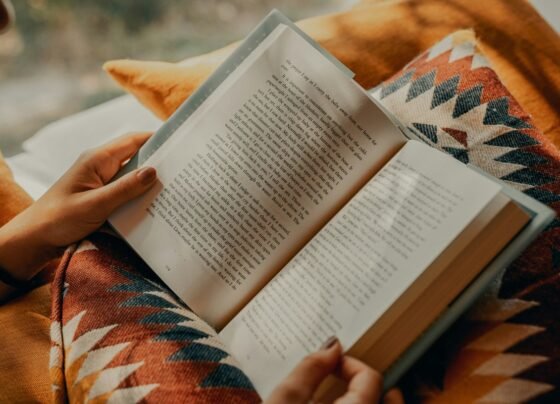 Imagem colorida de uma pessoa sentada no chão lendo um livro - Metrópoles