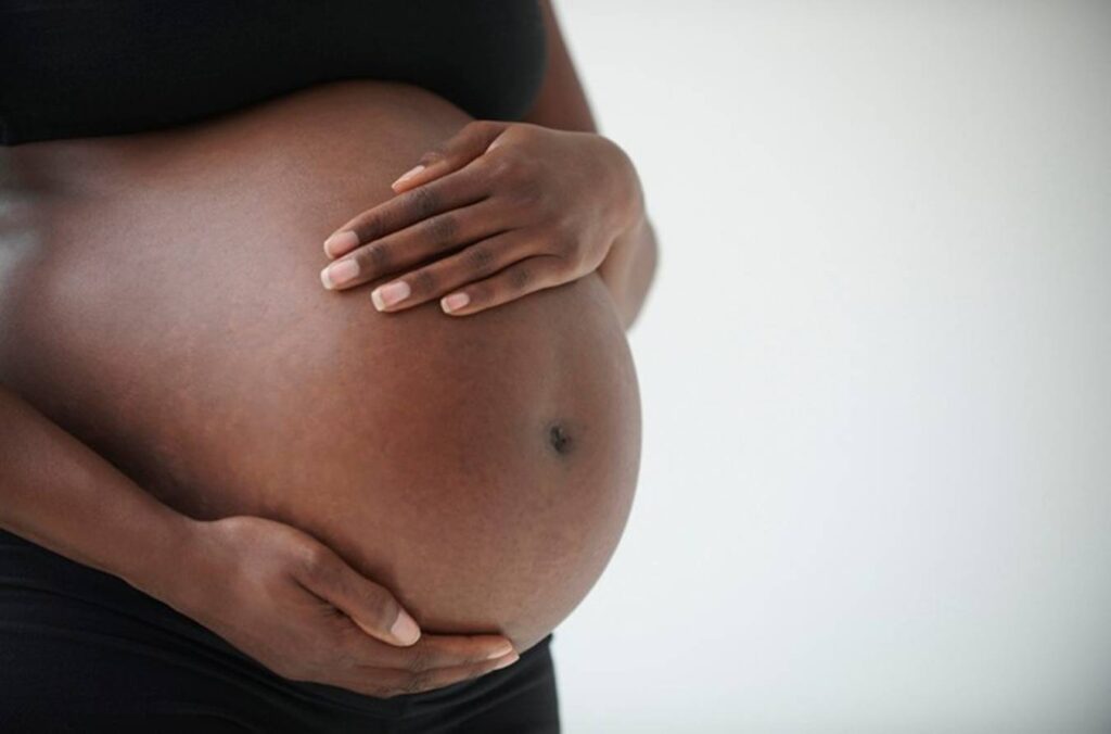 Imagem colorida: mulher preta grávida com mãos na barriga - Metrópoles