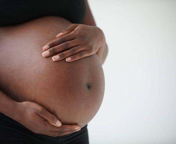 Imagem colorida: mulher preta grávida com mãos na barriga - Metrópoles