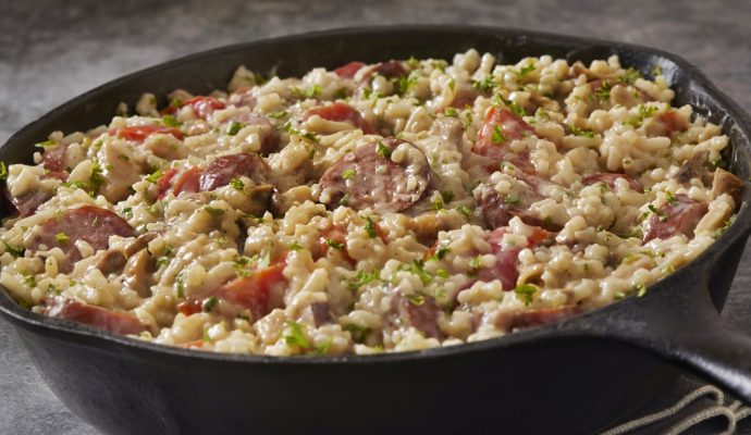 Foto colorida de arroz cremoso com diversos temperos e linguiça calabresa em panela